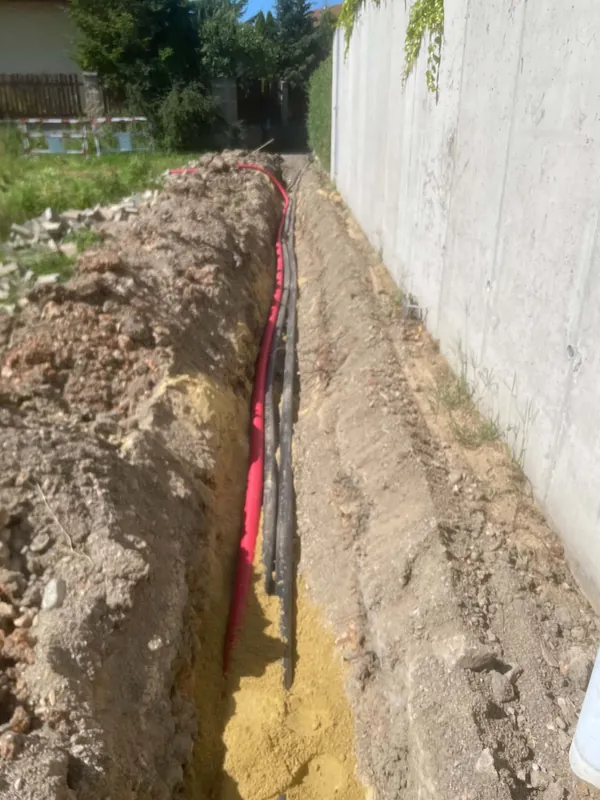 Rýha u betonové zdi s uloženými kabely v červené a černé chráničce