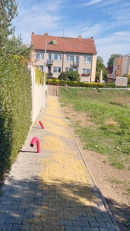Hotový chodník ze zámkové dlažby podél zdi, z okraje vyčnívají červené chráničky