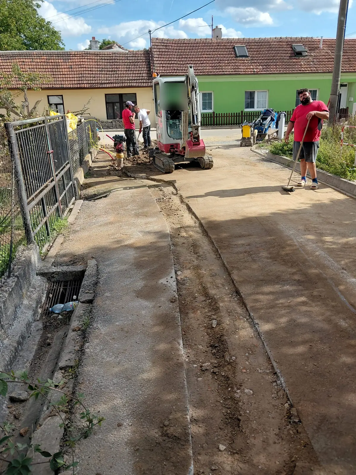 Malé rypadlo a lidé při výkopu v ulici