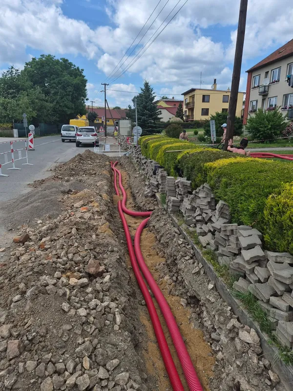 Červené chráničky ve výkopu podél ulice