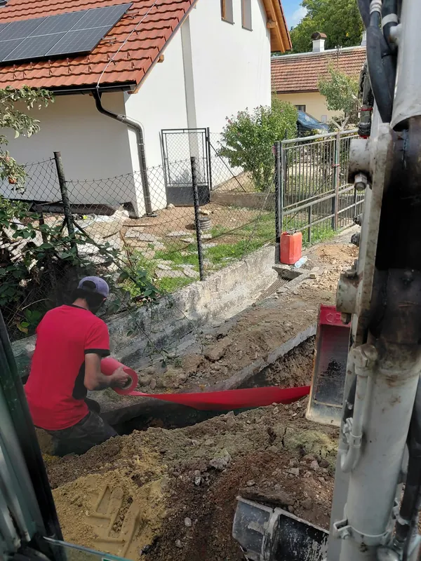 Pracovník ve výkopu protahuje červenou chráničku
