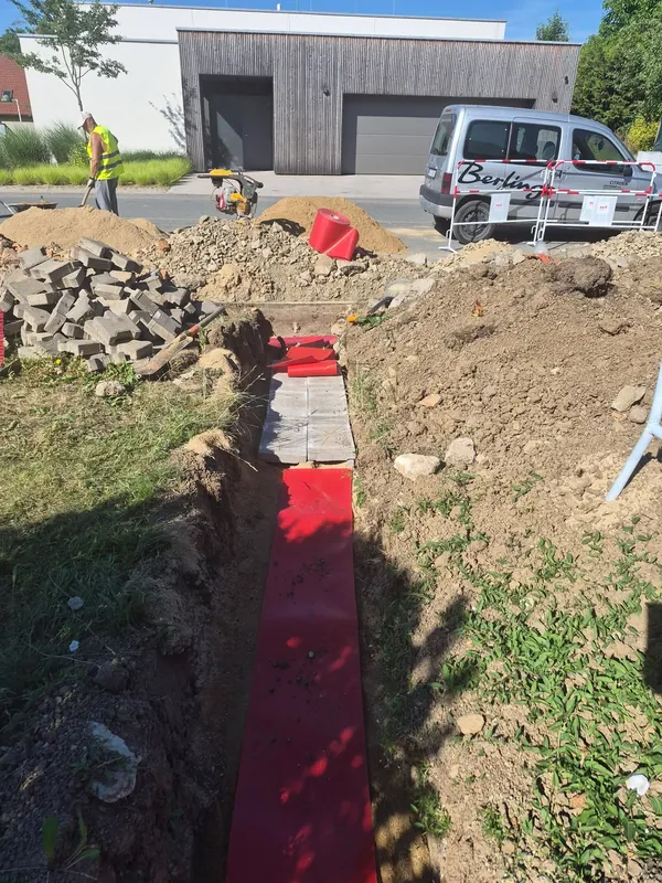 Rýha s červenou výstražnou fólií a dlaždicemi u rodinného domu